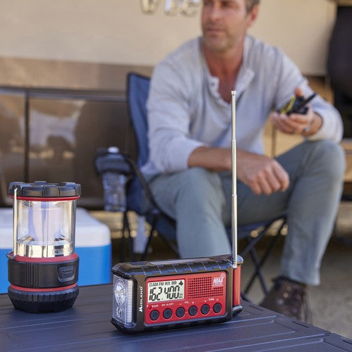 
                  
                    Emergency hand crank radio with flashlight and digital display on outdoor table.
                  
                
