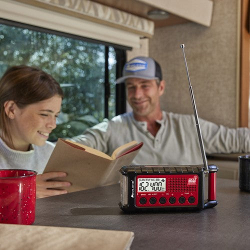 
                  
                    Midland ER310 Emergency Hand Crank Radio with flashlight on a table, people in background.
                  
                